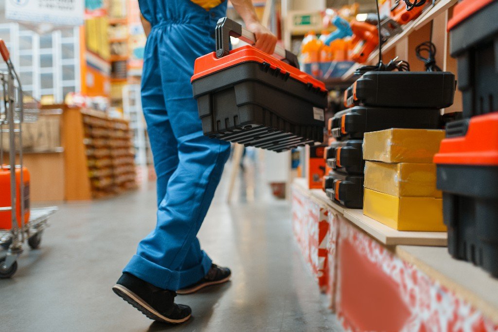 Male builder with toolbox at the shelf in hardware store. Constructor in uniform look at the goods in diy shop